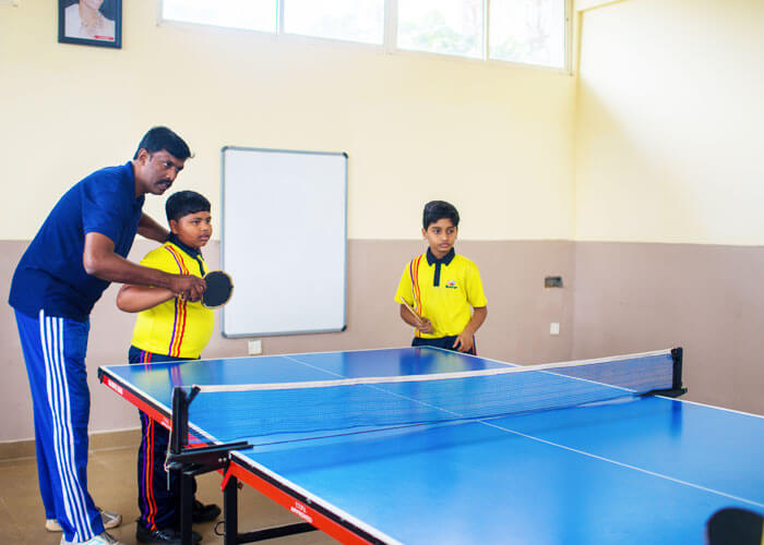 Teacher guiding students during a table tennis practice session at NewAge World School.